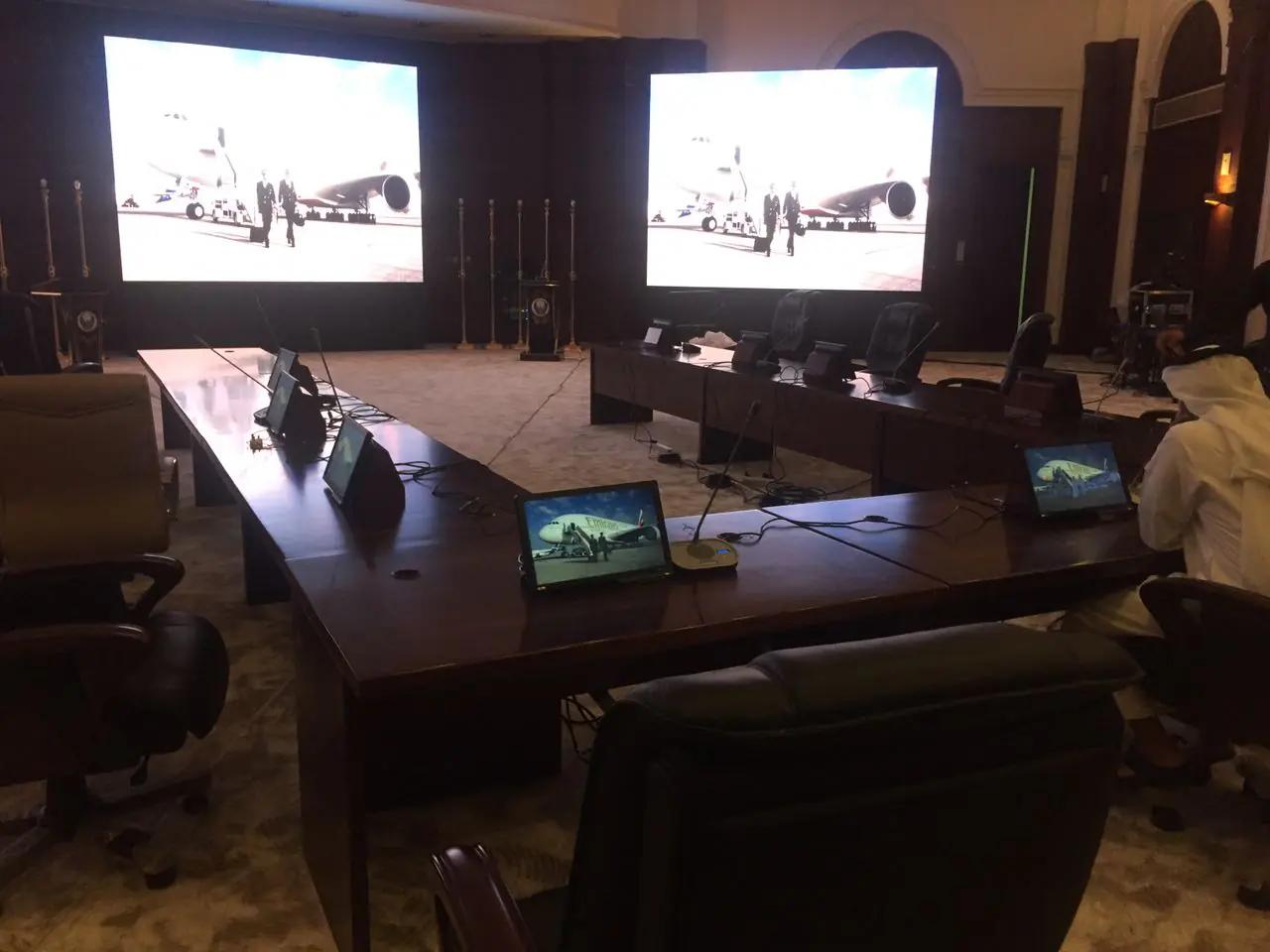 Conference room arranged around three synchronized presentation screens.