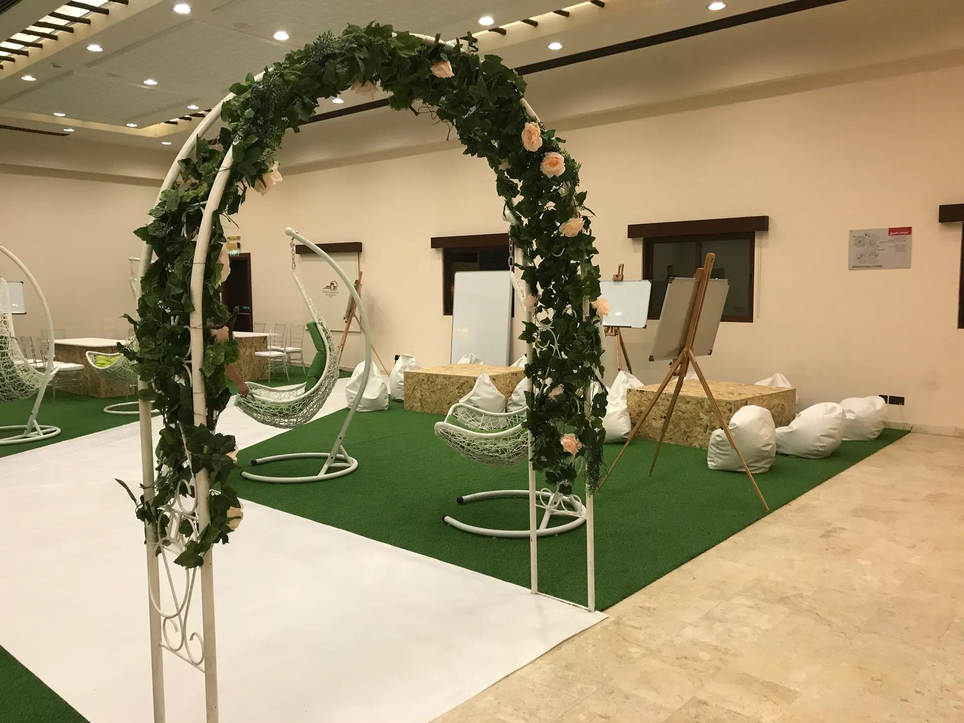 Interactive environment with a floral arch, suspended seating and workshop tables.