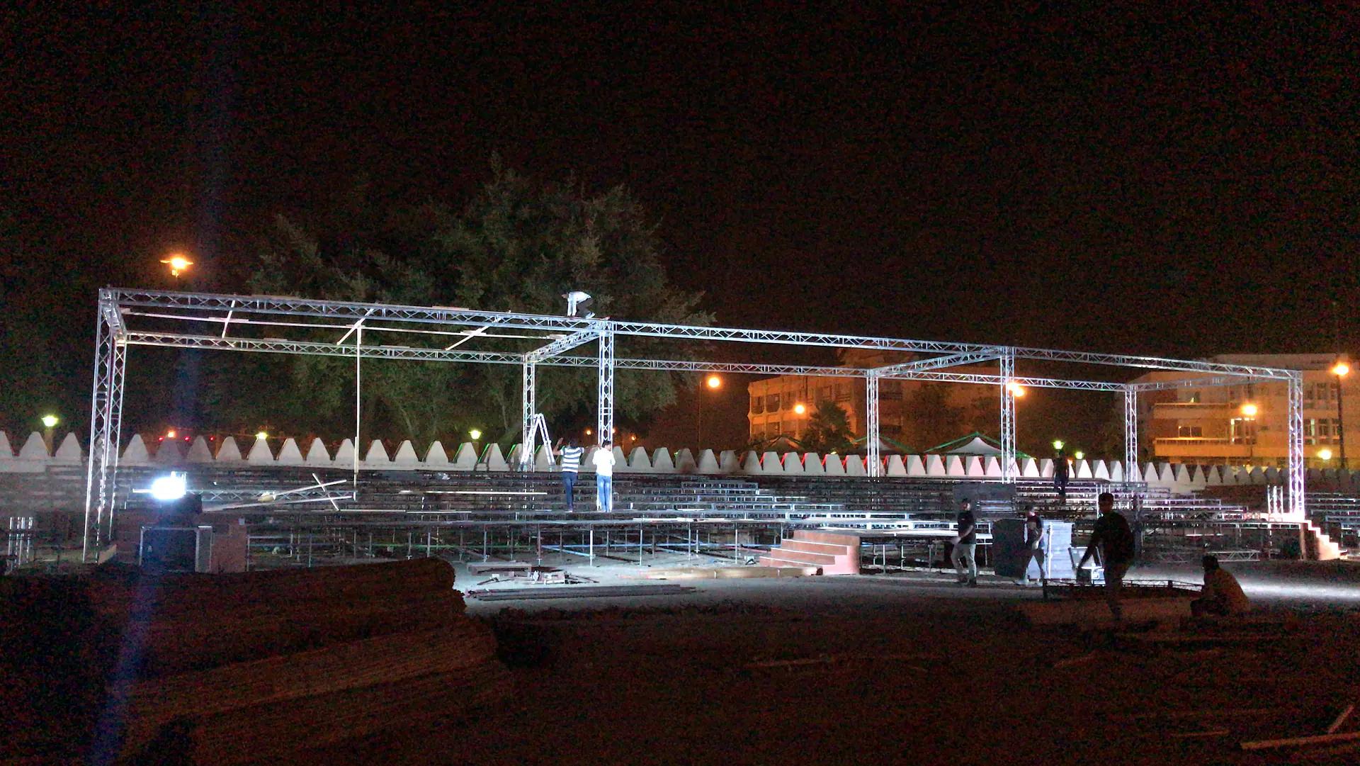 Outdoor truss structure and stepped audience platform during technical installation.