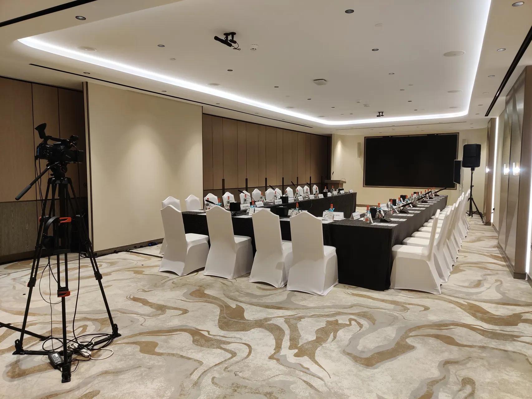Broadcast camera on a tripod positioned for a hybrid meeting setup
