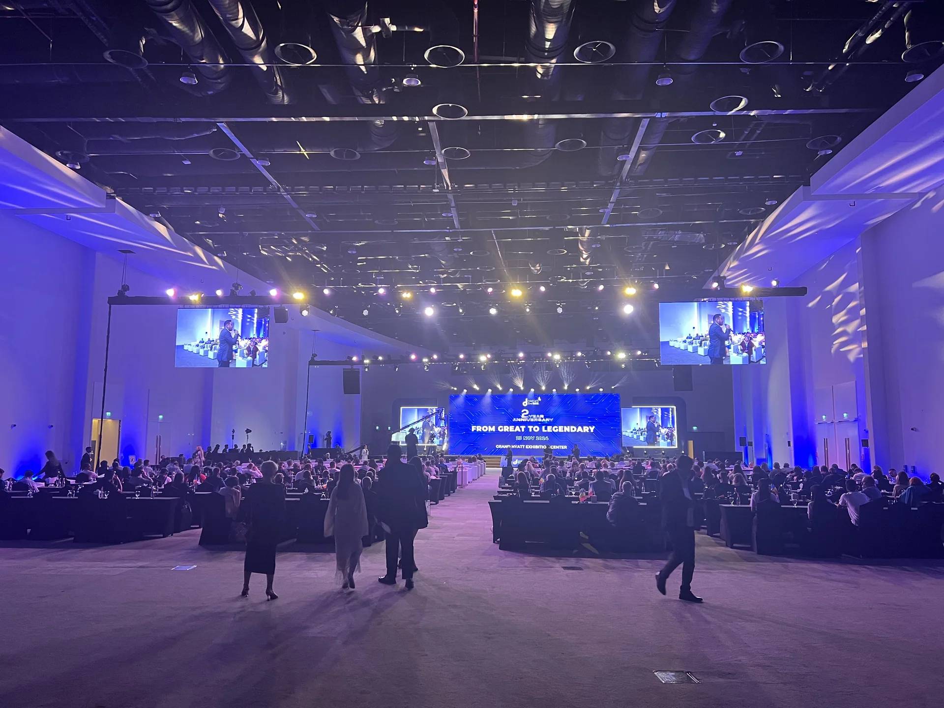 Large conference hall with delegate seating, an illuminated stage and suspended screens
