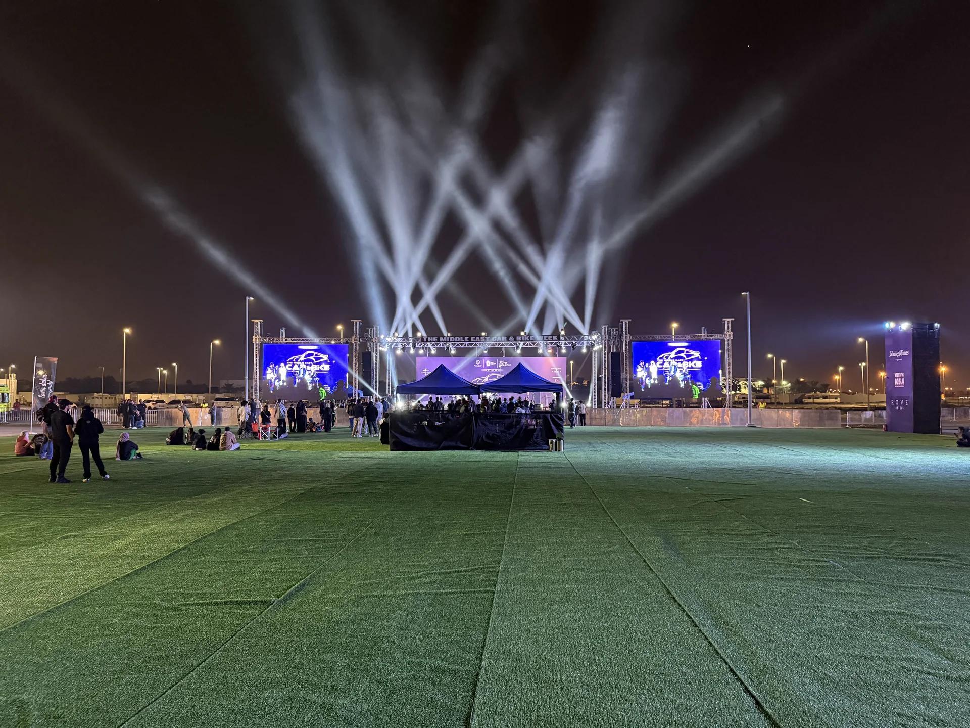 Outdoor festival environment with stage screens and programmed beams of light.